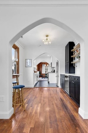 Una cocina con armarios blancos, piso de madera y una araña.