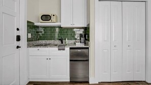 Une cuisine avec des meubles blancs, un crédence en carreaux verts, un réfrigérateur en acier inoxydable et une porte blanche.