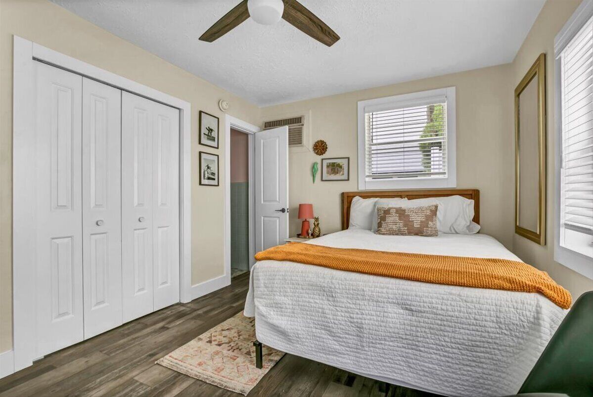 Un dormitorio con cama, ventilador de techo, ventana con persianas y una puerta.