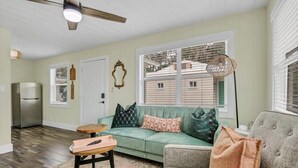 A living room with a green sofa, a grey armchair, a woven ottoman, and a small wooden table.