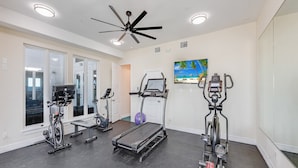 Ein Fitnessraum mit Laufbändern, Crosstrainern und einem Deckenventilator.