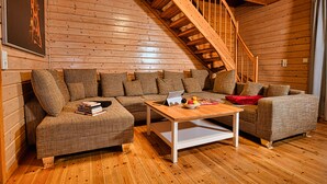 Une pièce chaleureuse avec un escalier en bois, un ensemble de canapés et une table basse sur laquelle sont posés des livres et des fruits.