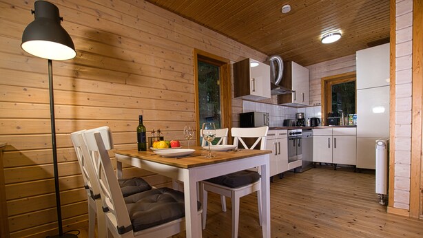 L’intérieur d’une cabane en bois comprend une table à manger, des chaises, une lampe sur pied et un coin cuisine.