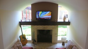 Ein Wohnzimmer mit Kamin, Fernseher und Gitarre.