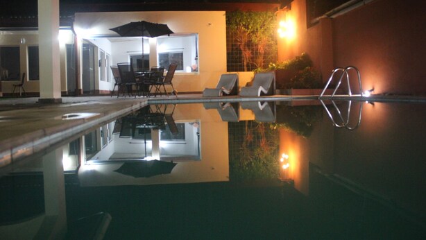 Ein Pool im Freien mit Liegestühlen und einem Tisch unter einem Sonnenschirm, der die Umgebung spiegelt.