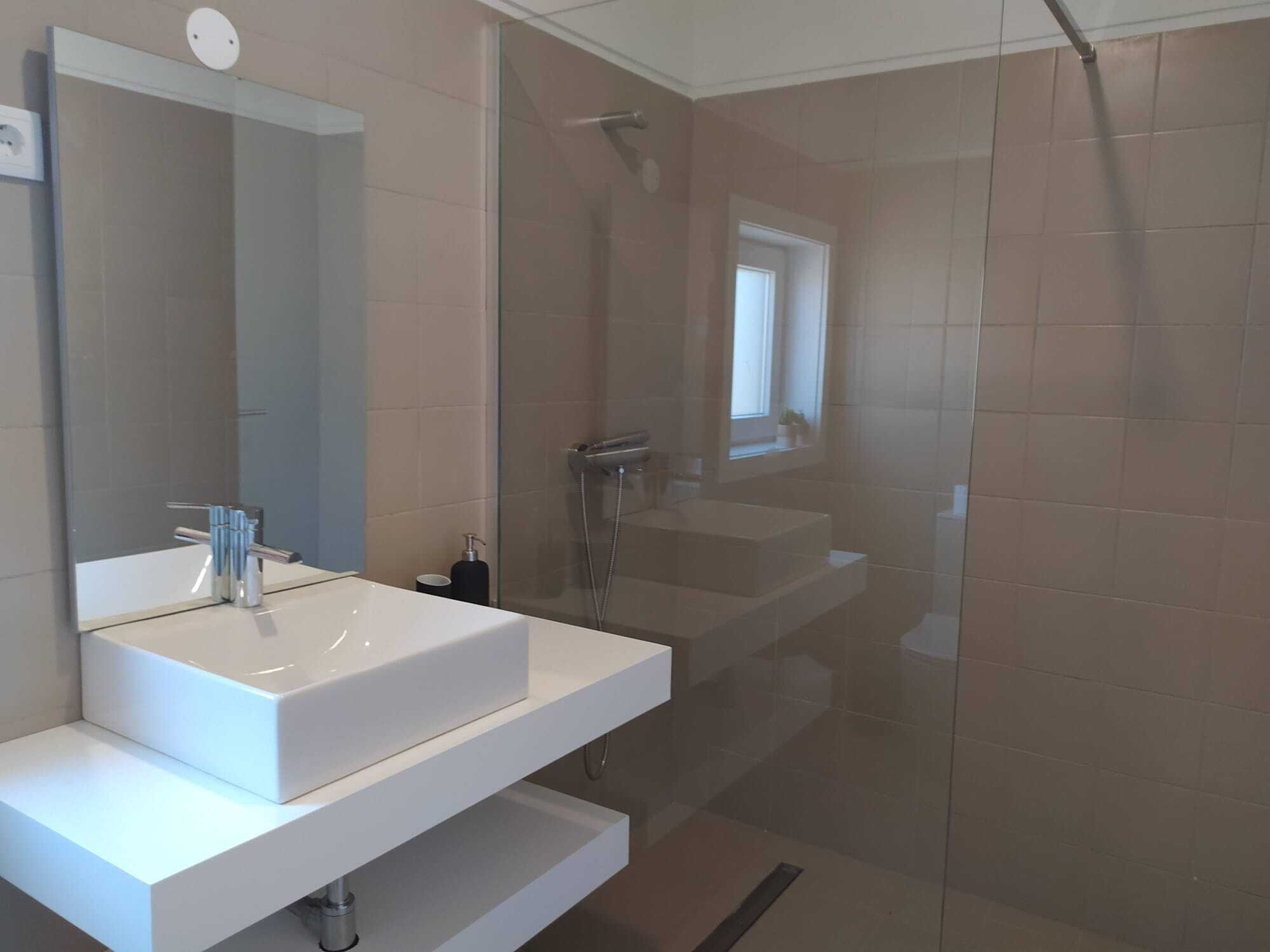 Une salle de bain moderne avec un grand miroir, un lavabo blanc et une douche séparée par une paroi de verre.
