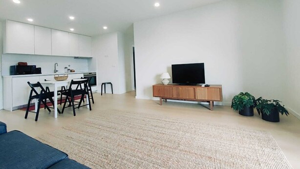 Een moderne woonkamer met een flatscreen televisie, een houten kast en een eethoek met een tafel en stoelen.