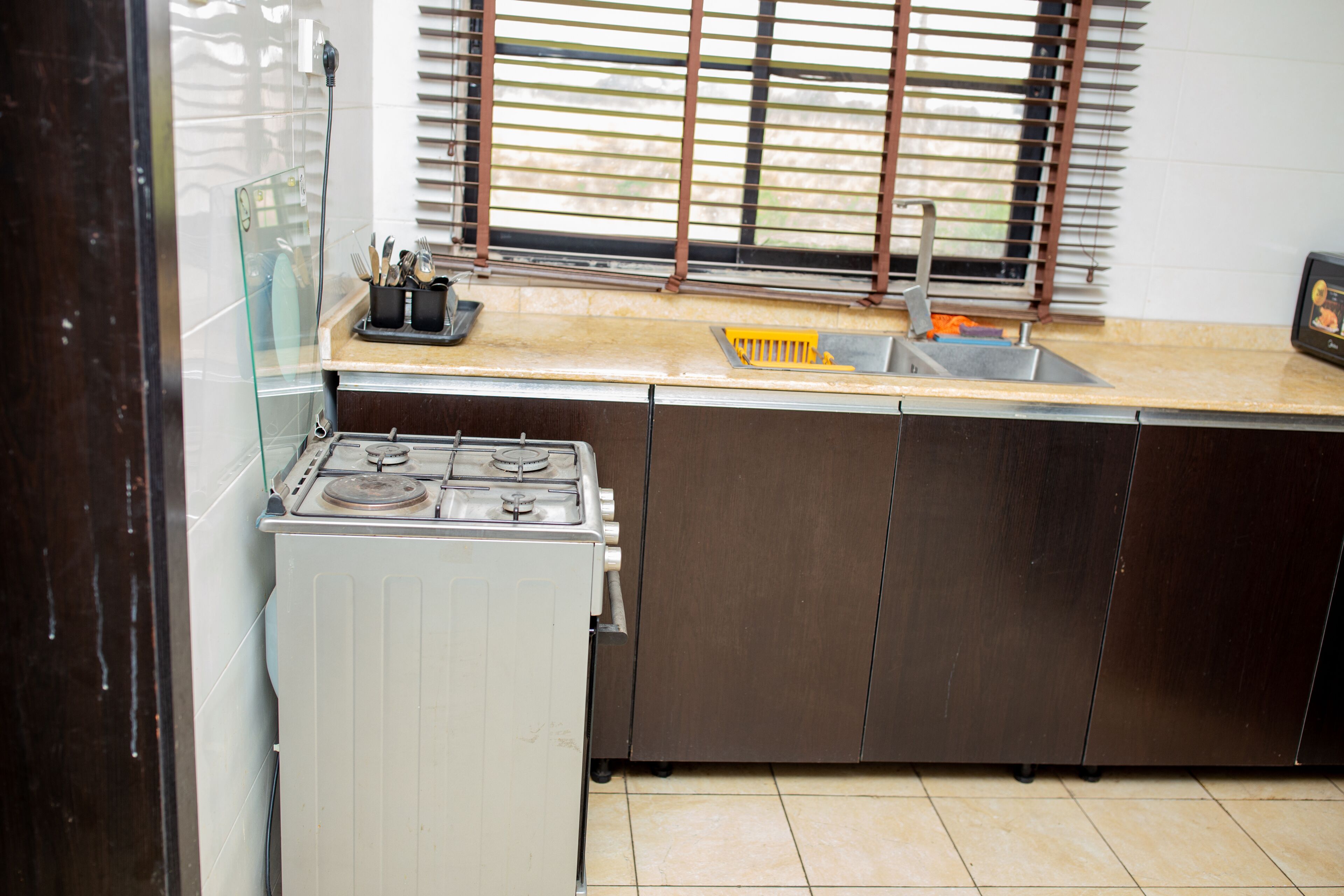 A kitchen with a stove, sink, and window blinds.