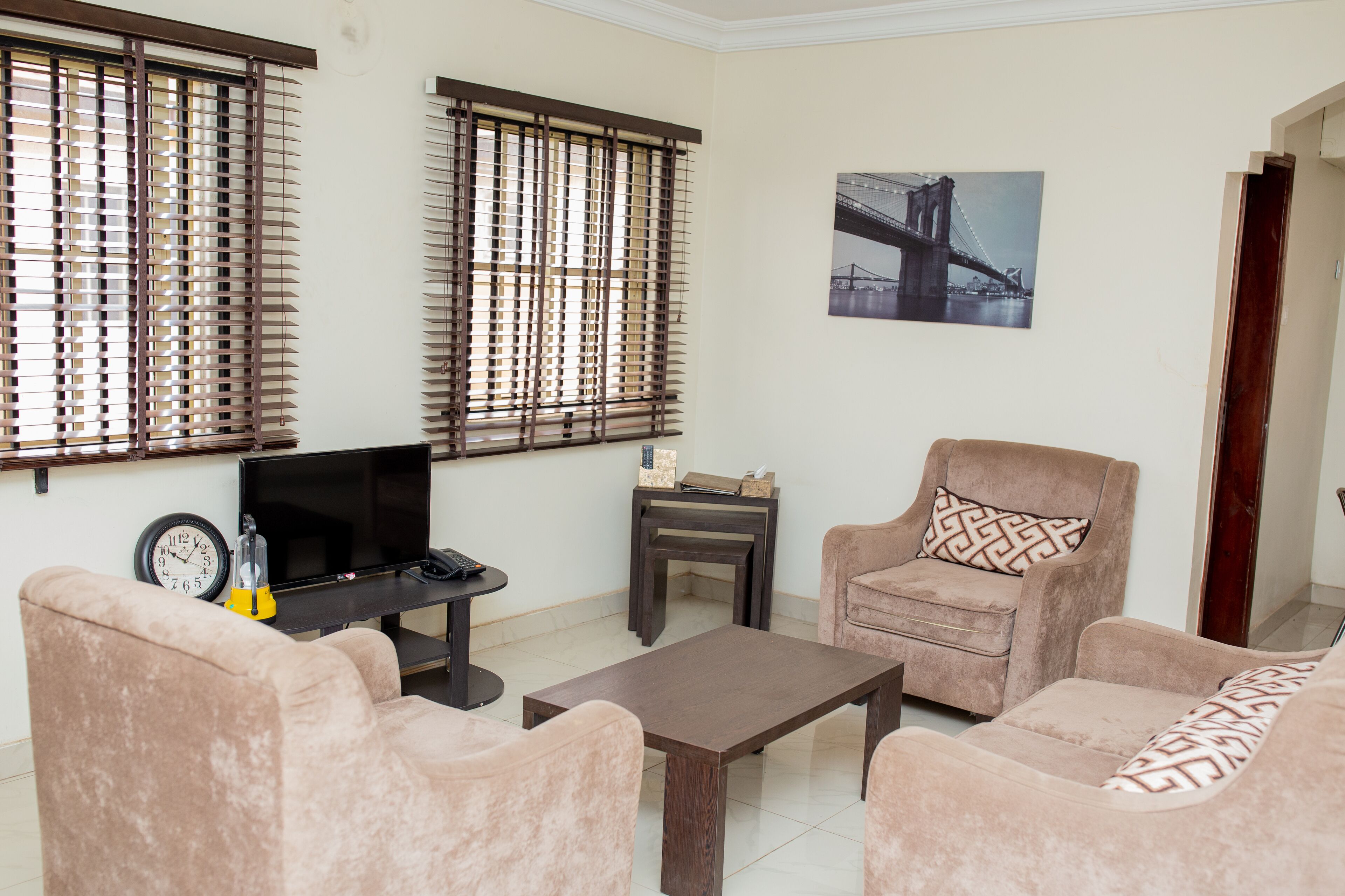 A living room with beige sofas, a coffee table, a TV, and a clock.