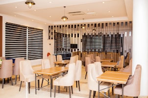 Un comedor moderno con mesas y sillas, un muro decorativo y un amplio ventanal con persianas.
