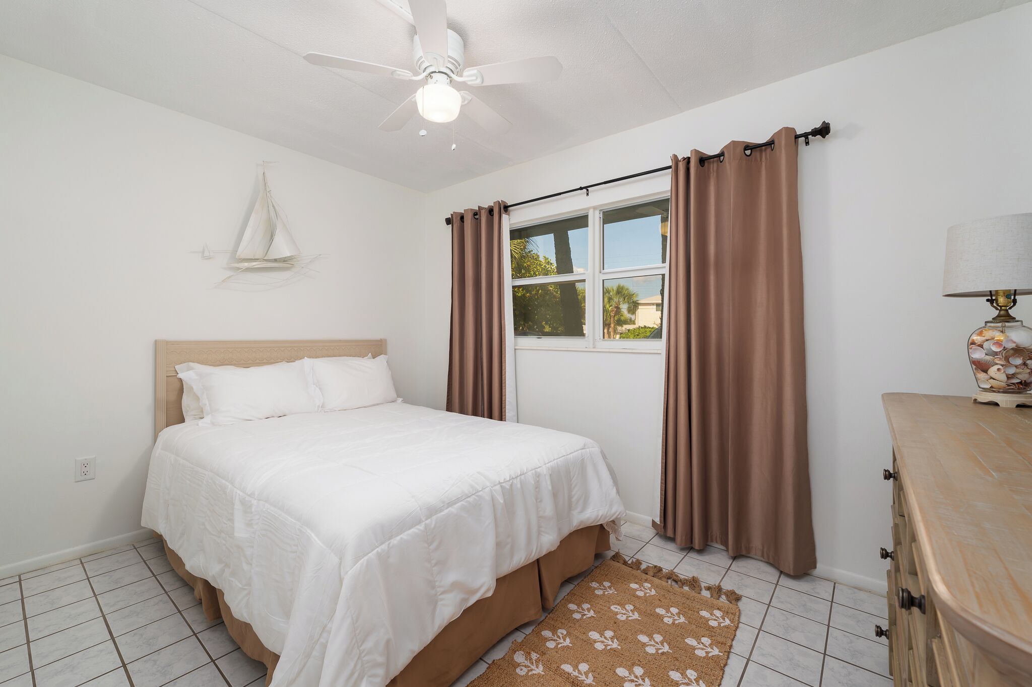 A bedroom with a bed, a ceiling fan, a window with curtains, and a dresser.