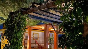Un espace extérieur accueillant, aménagé avec des sièges confortables et un hamac, entouré d’une végétation luxuriante et agrémenté d’une pergola en bois.