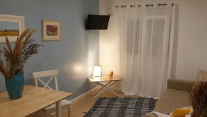 Une pièce chaleureuse avec une table en bois, une chaise, une petite table avec une lampe, un canapé et un téléviseur fixé au mur.
