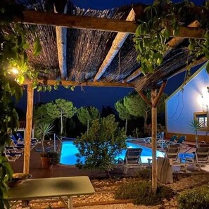 A nighttime outdoor pool area with lounge chairs and a pergola structure.