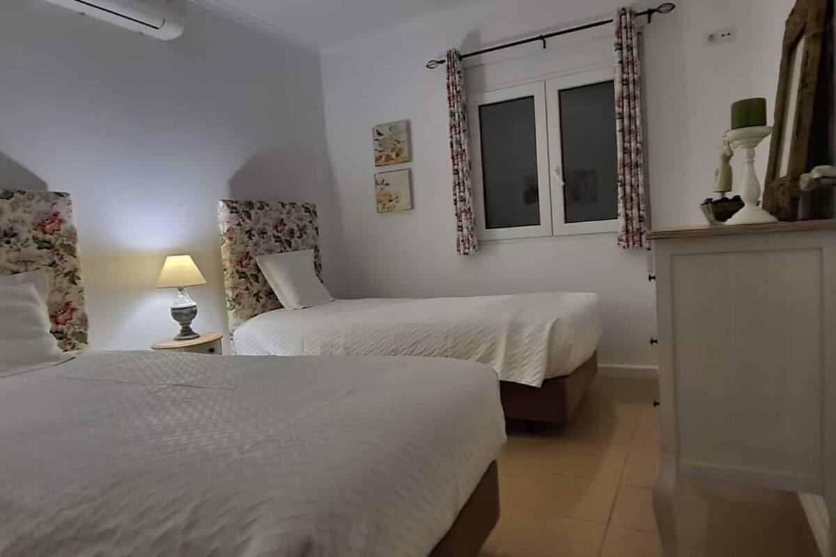 Une chambre avec deux lits, une table de chevet avec une lampe, une fenêtre avec des rideaux et un miroir au mur.