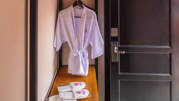 Une chambre d’hôtel avec un banc en bois, un peignoir suspendu à un porte-manteau et des chaussons posés sur le sol.