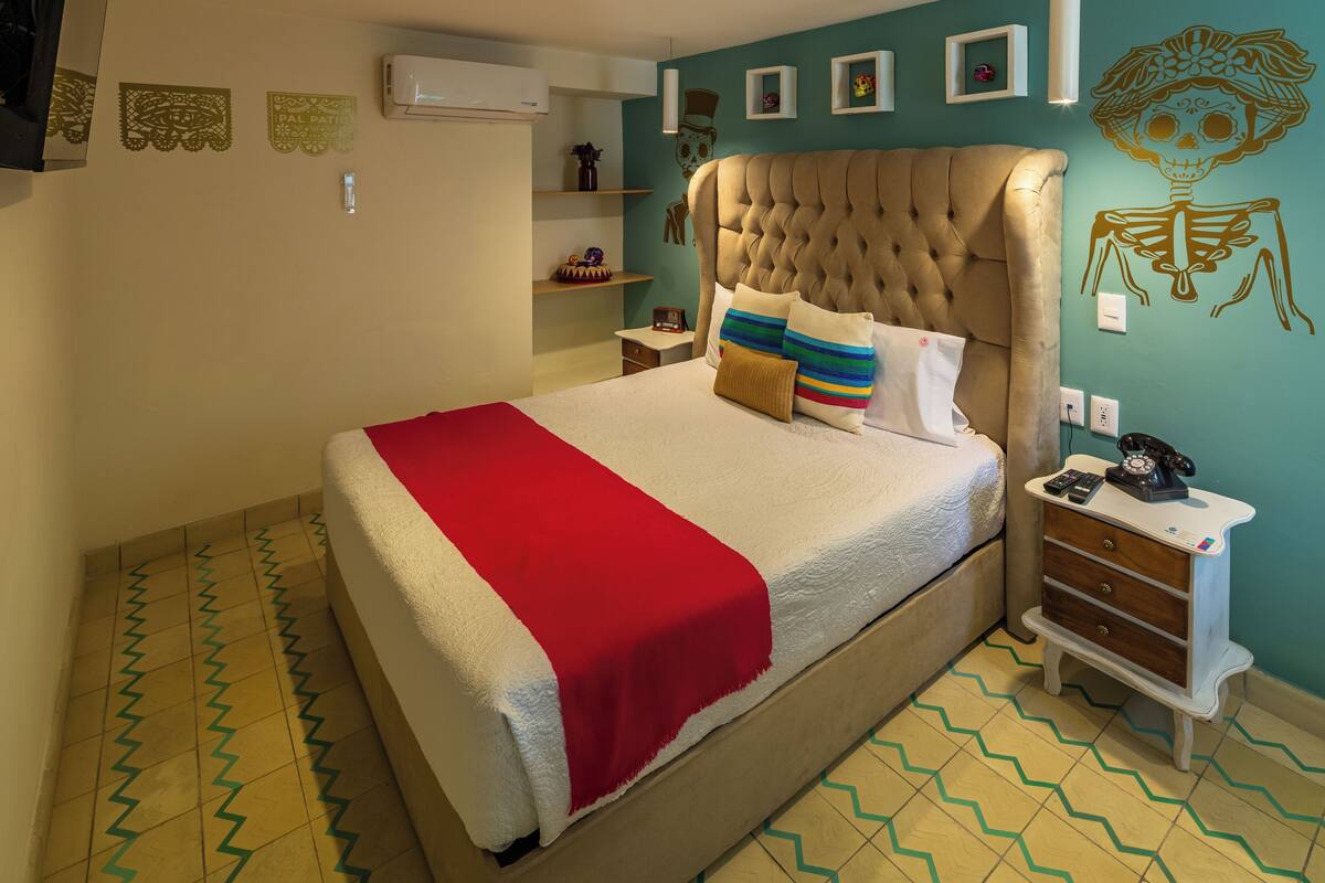 A bedroom with a large bed, a nightstand, a wall-mounted air conditioner, and decorative wall art.
