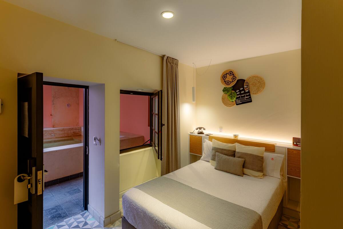 A hotel room with a bed, a bedside table, a telephone, and a wall-mounted clock.