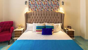 A bedroom with a large bed, a red armchair, a colorful wall hanging, and a nightstand with a radio.