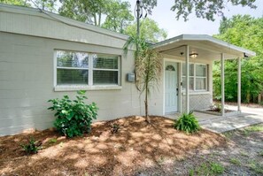 Stroll through the serene garden, surrounded by lush greenery and a shaded tree, to the inviting front porch with a covered area.