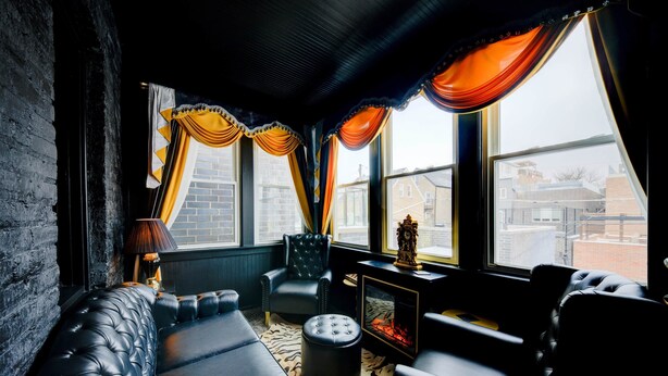 Une pièce chaleureuse avec une cheminée, des fauteuils en cuir et de grandes fenêtres ornées de rideaux.
