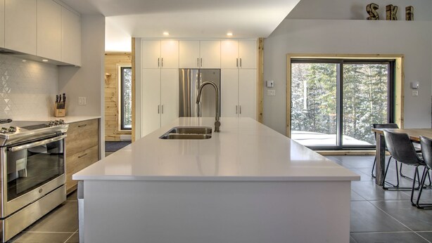 A modern kitchen with a central island, stainless steel appliances, and a view of a snowy landscape through large windows. - Chalet Haut-Bois | Hiking, Skiing & Spa (Morin-Heights)