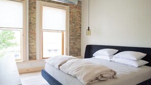 A bedroom with a bed, a window, a brick wall, and a hanging light fixture. - Flat 304 Front and Union (Traverse City)