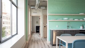 A modern kitchen with a stainless steel dishwasher, a sink, and a countertop with glassware. There is a dining table with chairs and a view of the city through a large window. - Flat 304 Front and Union (Traverse City)