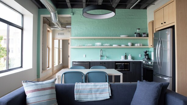 A modern kitchen with teal brick backsplash, stainless steel appliances, and a dining area with blue chairs. - Flat 304 Front and Union (Traverse City)