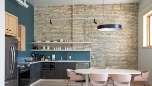 A modern kitchen with a brick wall, stainless steel appliances, and a round dining table with chairs. - Flat 203 Front and Union (Traverse City)