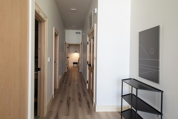 A hallway with wooden flooring, a black metal shelf unit, and a wall-mounted artwork.