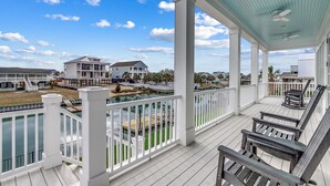 A covered porch with white railings, wooden benches, and a view of the beach and houses. - Inlet Oasis - Creekfront in Garden City (Garden City Beach)