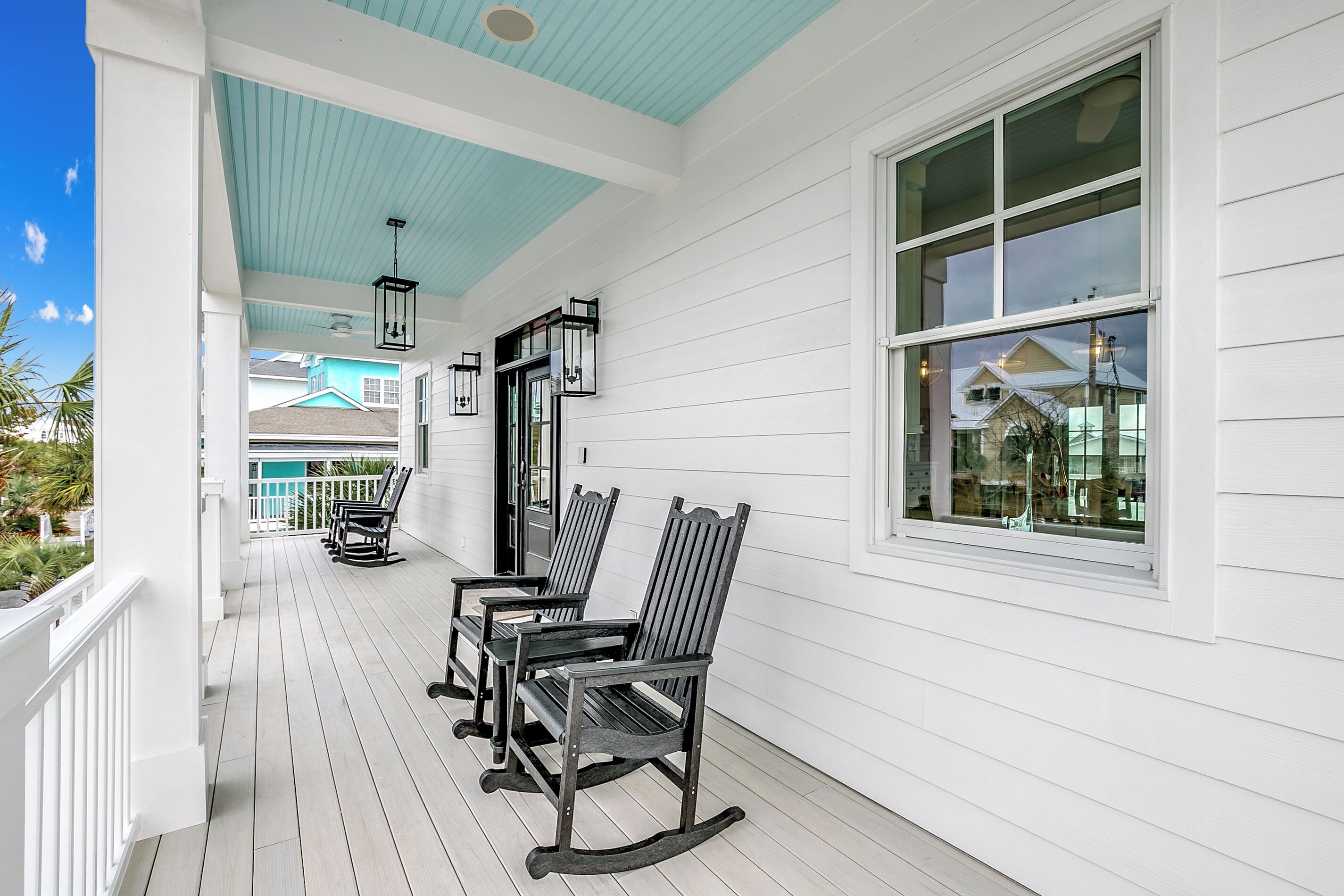 A covered porch with white railings, rocking chairs, and a large window.