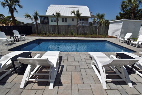 Une piscine entourée de chaises longues blanches et d’une terrasse en bois.