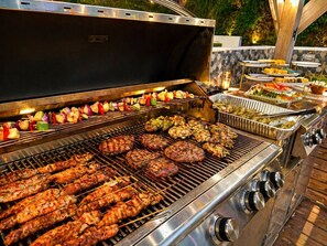 Un barbecue avec des brochettes de viande et de légumes, un grill doté de plusieurs surfaces de cuisson et un buffet proposant divers plats.