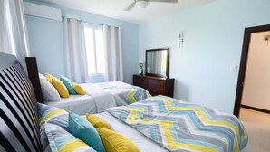 Quarto com duas camas, cômoda, espelho e janela com cortinas.