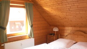 Una habitación de madera con una cama, una mesita de noche, una lámpara y una ventana con cortinas.
