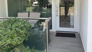 Une entrée moderne avec une porte en verre, un petit espace extérieur aménagé avec des coussins et une plante en pot.
