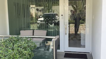 A modern entrance with a glass door, a small outdoor seating area with cushions, and a potted plant.
