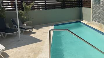 A rectangular swimming pool with a metal safety railing, surrounded by lounge chairs and a pergola.