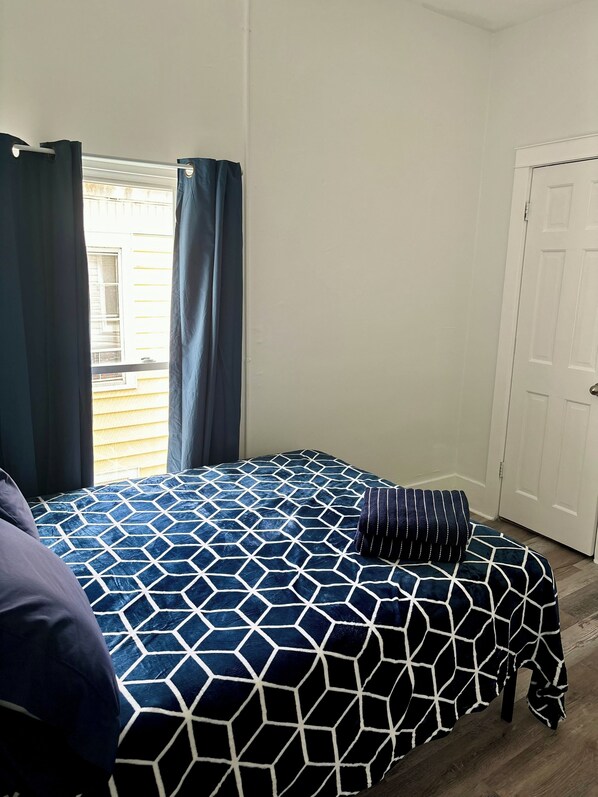 A bedroom with a bed covered in a geometric patterned bedspread, a dark blue curtain, and a white door. - Great house for groups! (Oneonta)