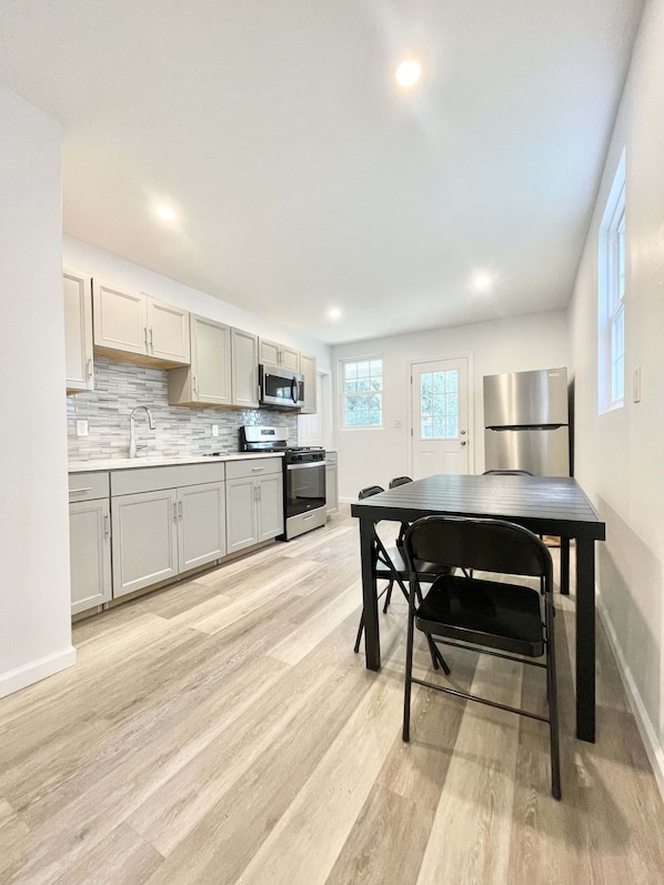 A modern kitchen with light wood flooring, white cabinets, stainless steel appliances, and a dining area with a table and chairs. - Great house for groups! (Oneonta)