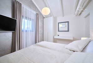 Relax in a serene space with a large bed, flat-screen TV, and natural light pouring in through sheer curtains.