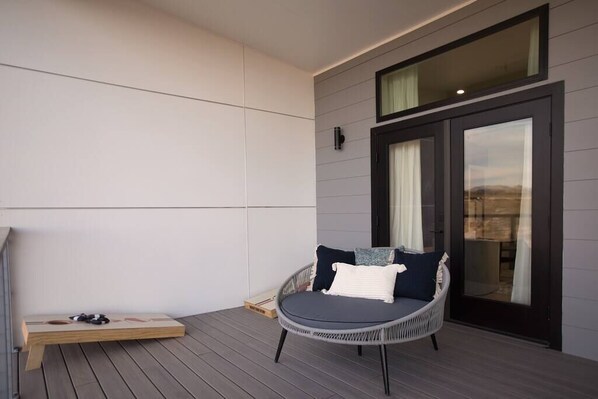 Un espace extérieur moderne, aménagé avec des meubles de jardin, comprenant un fauteuil en osier et une table en bois, une porte-fenêtre coulissante et une vue sur le paysage.