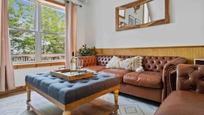 Un salón con un sofá de cuero marrón, un reposapiés tapizado en azul y una mesa de centro de madera.