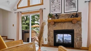 Una sala de estar acogedora con muebles de mimbre, una chimenea de piedra y un amplio ventanal con vistas al exterior.
