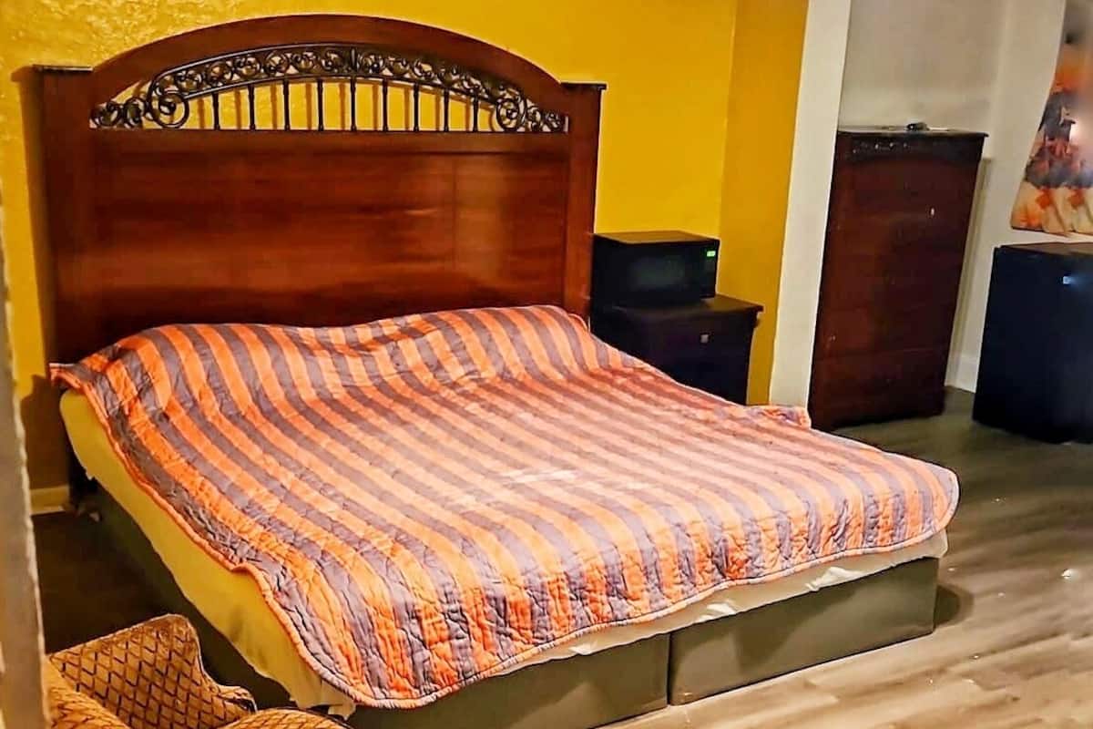 Une chambre à coucher avec un lit en bois, une petite table de chevet, une chaise et un ventilateur de plafond.