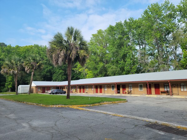 Un motel composé d’un bâtiment d’un seul étage, d  ’un parking et d’un espace verdoyant agrémenté de palmiers.