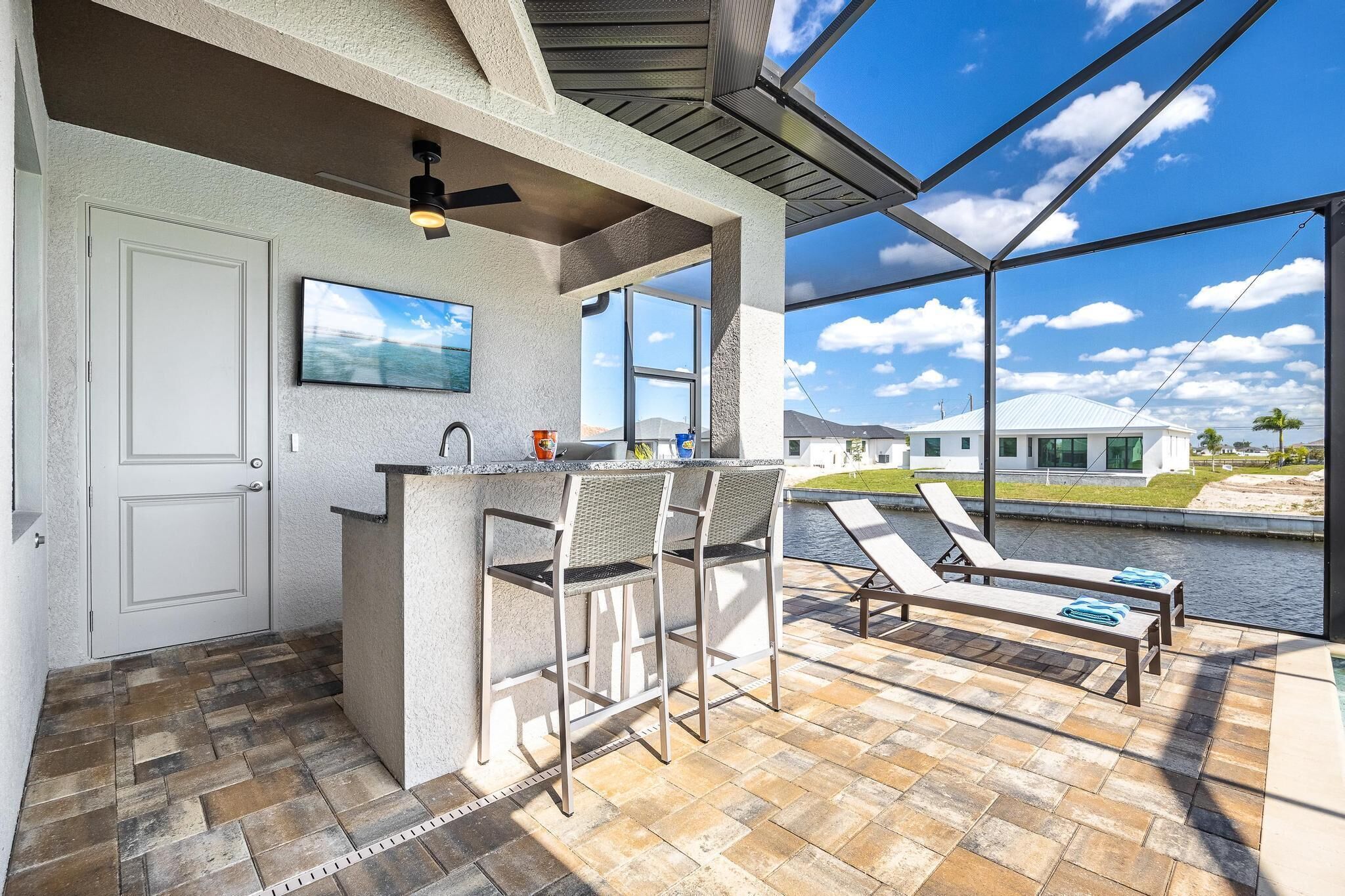 Un área de bar al aire libre con vista a la piscina, una puerta y un ventilador de techo.