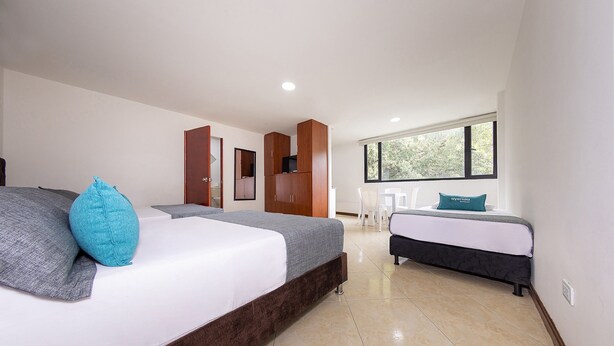 A modern bedroom with a large bed, a smaller bed, a wardrobe, and a window with a view of trees. - HOTEL LAURELES PALO ALTO (Medellín)